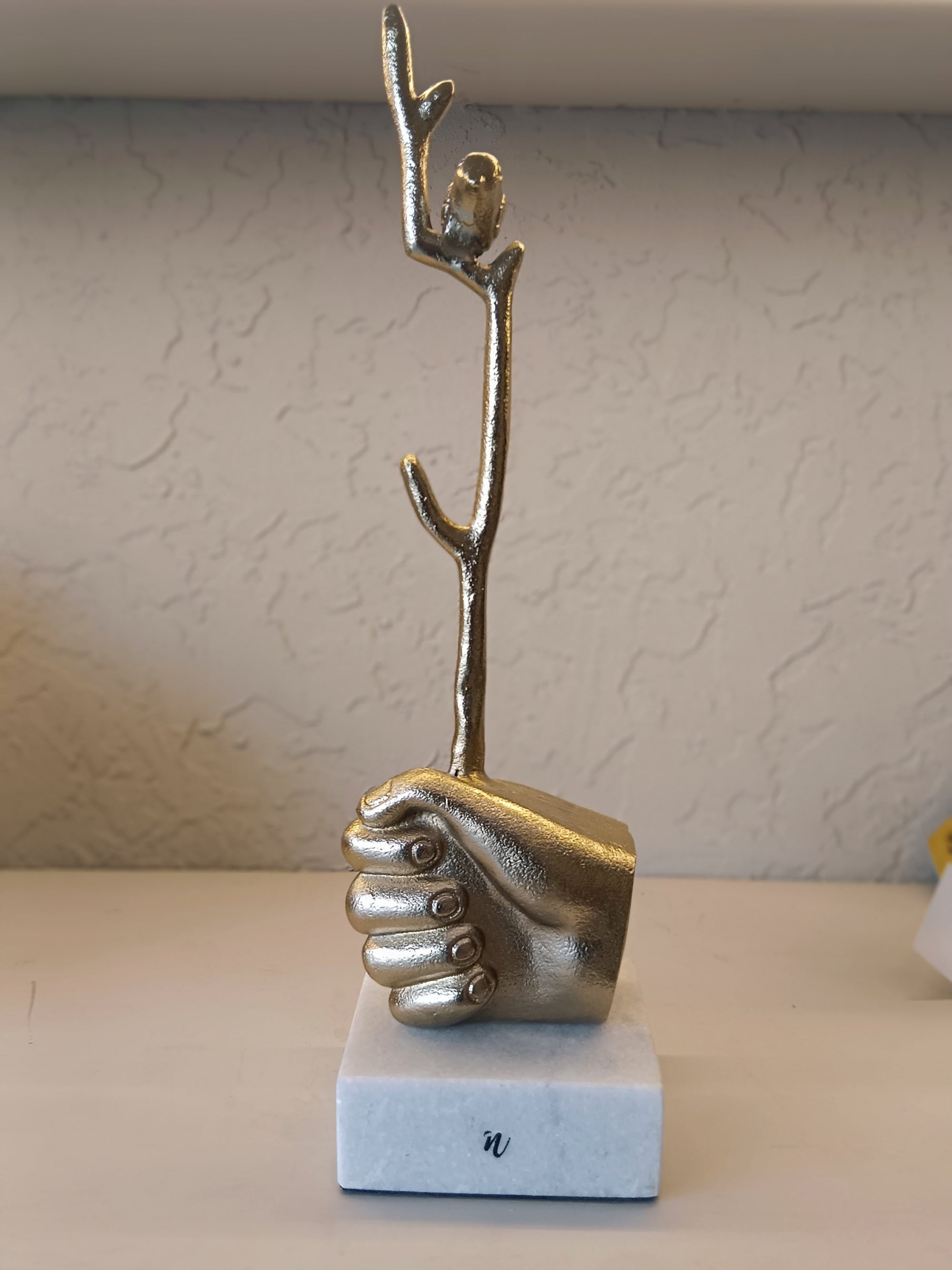 Golden Sculpted Hand Firmly Grasps A Bird On Top Of Branch