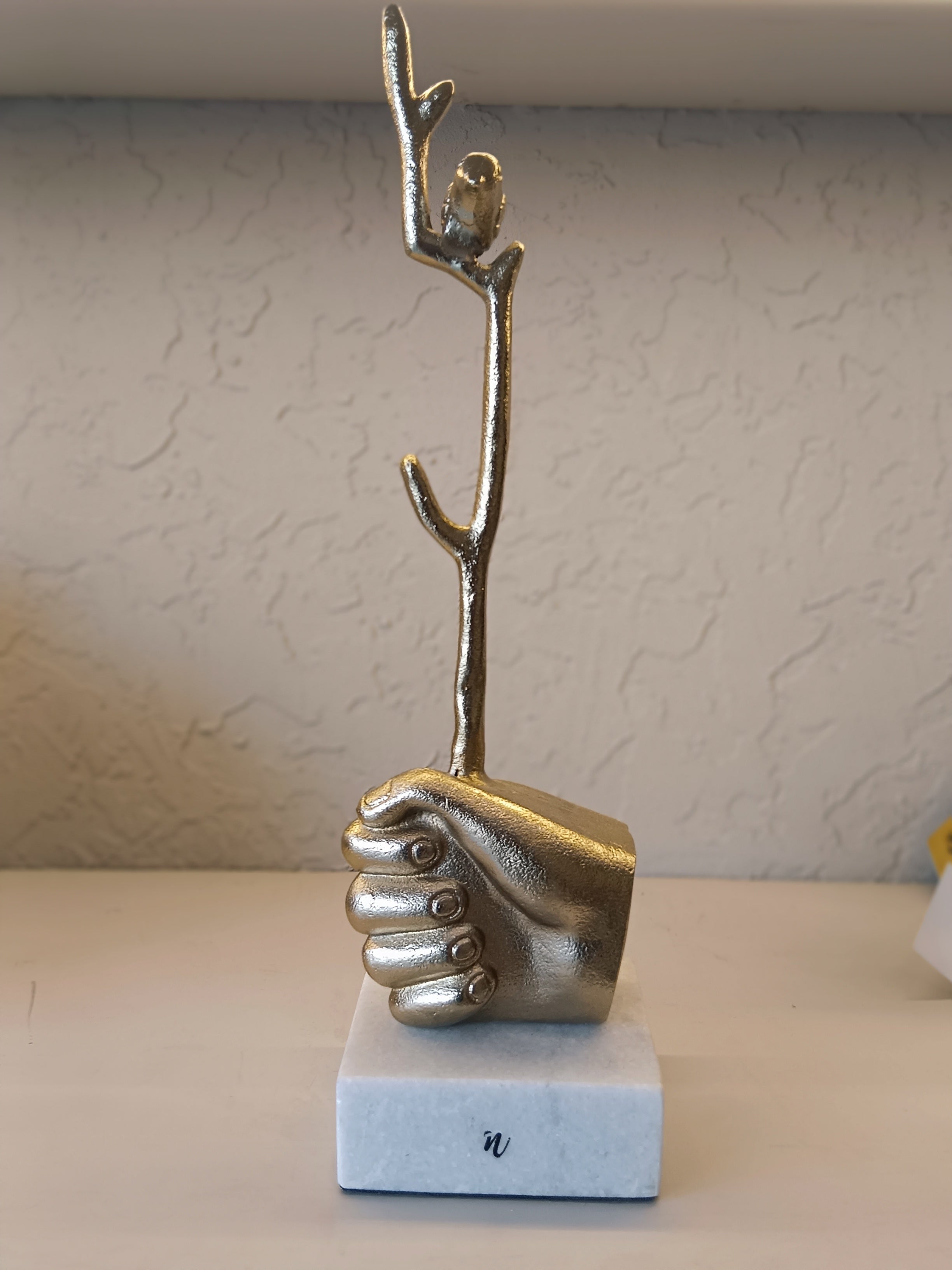 Golden Sculpted Hand Firmly Grasps A Bird On Top Of Branch