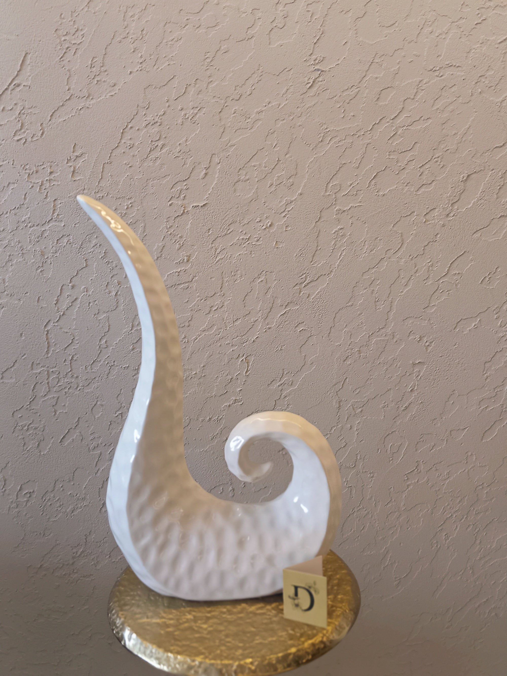 A Modern Abstract Ceramic Sculpture Featuring A Sleek, Spiral Horn-Like Design With A Hammered Texture In Glossy White Finish.