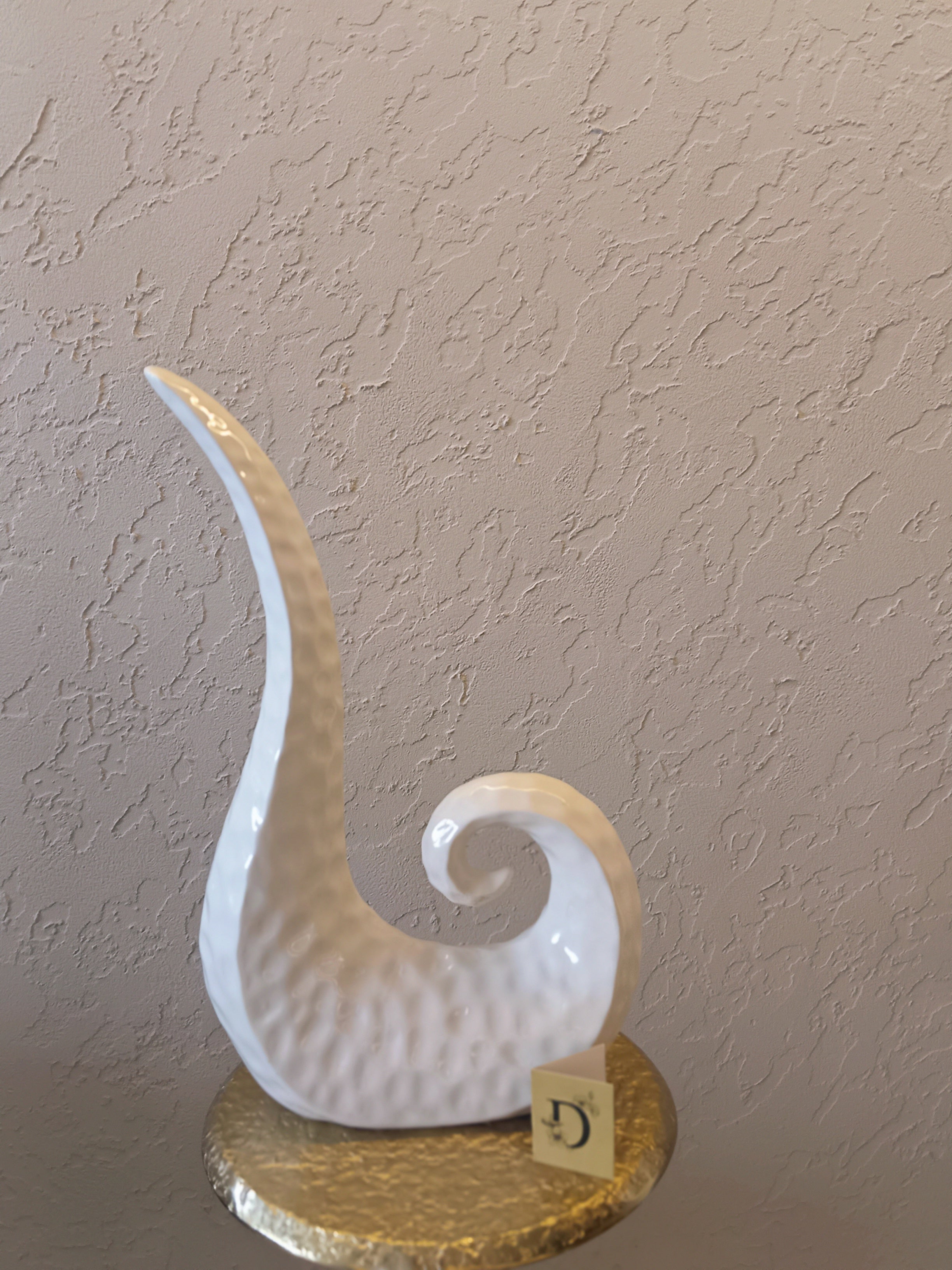 A Modern Abstract Ceramic Sculpture Featuring A Sleek, Spiral Horn-Like Design With A Hammered Texture In Glossy White Finish.