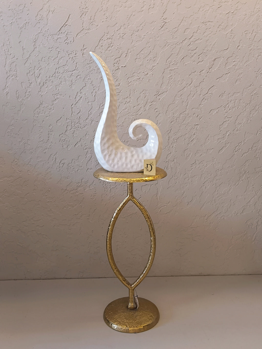 A Modern Abstract Ceramic Sculpture Featuring A Sleek, Spiral Horn-Like Design With A Hammered Texture In Glossy White Finish.