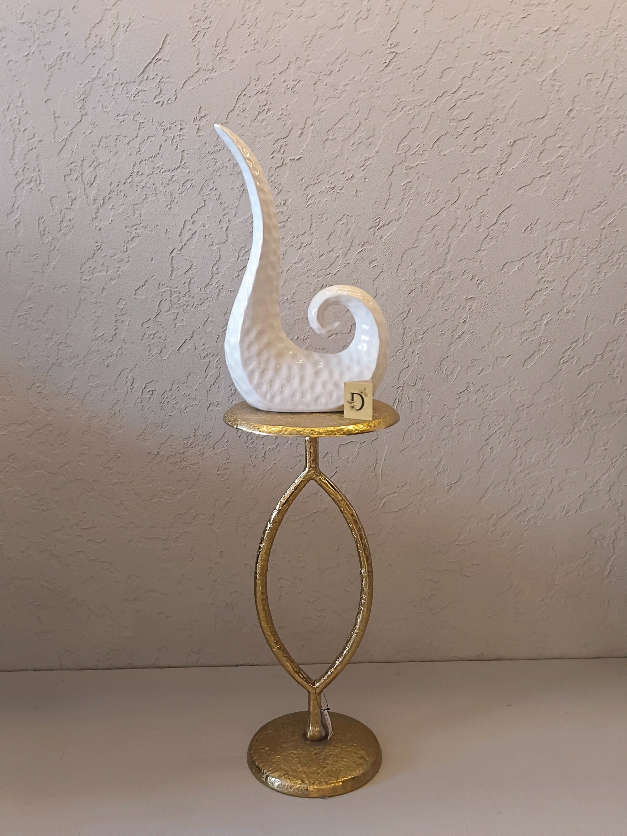 A Modern Abstract Ceramic Sculpture Featuring A Sleek, Spiral Horn-Like Design With A Hammered Texture In Glossy White Finish.