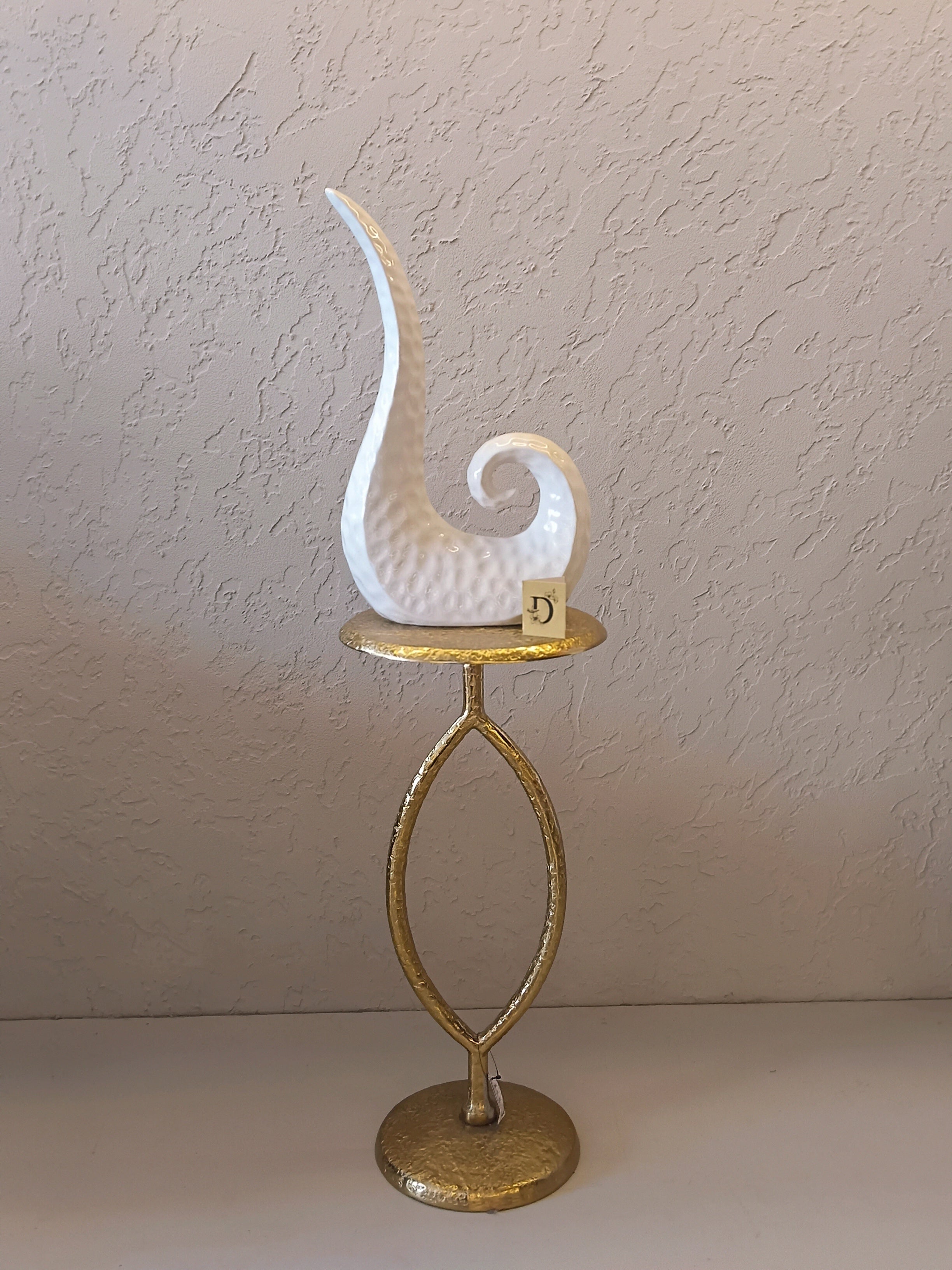 A Modern Abstract Ceramic Sculpture Featuring A Sleek, Spiral Horn-Like Design With A Hammered Texture In Glossy White Finish.