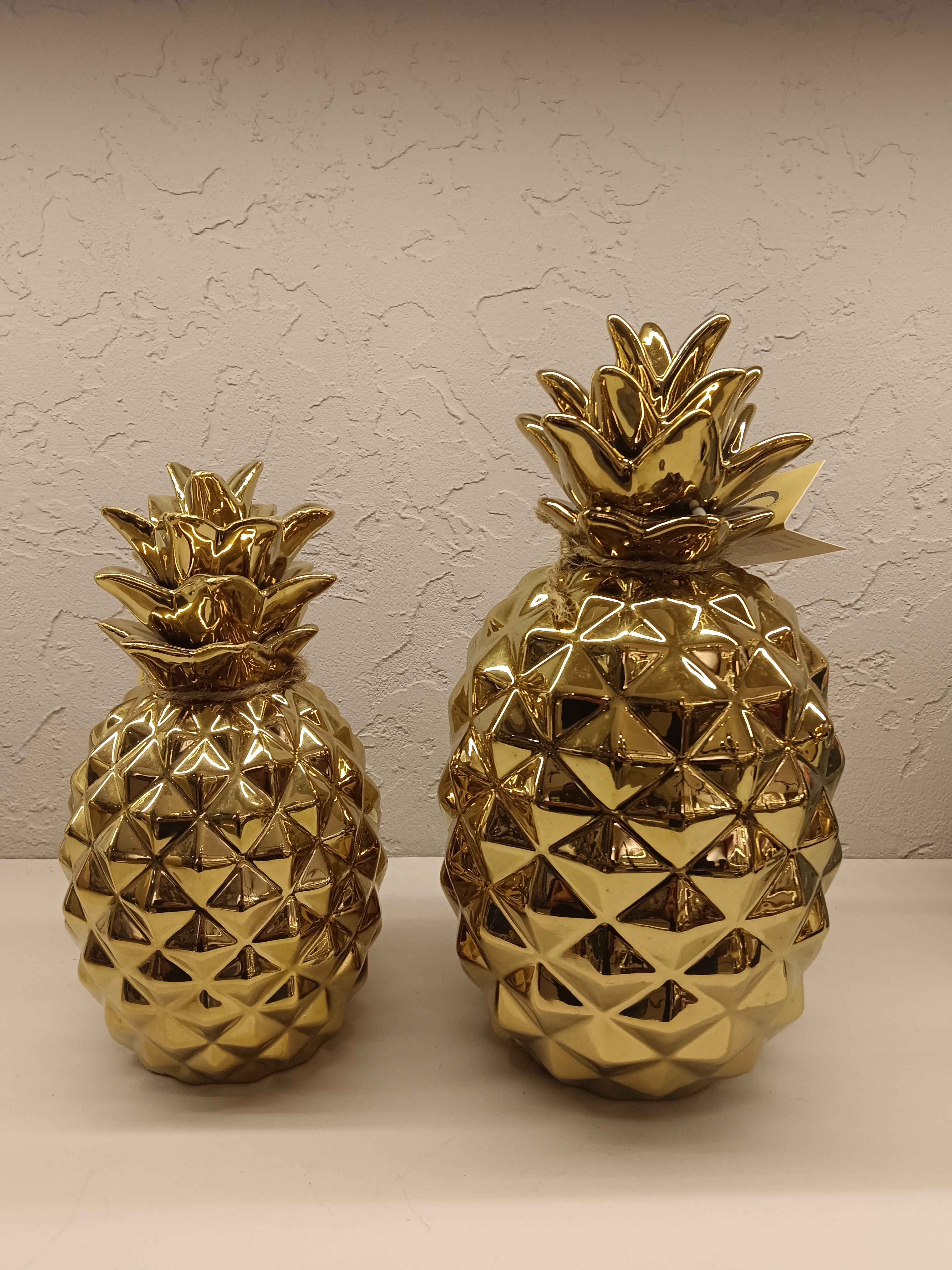 Two shiny, gold-finished ceramic pineapple figurines, each with a textured geometric design
