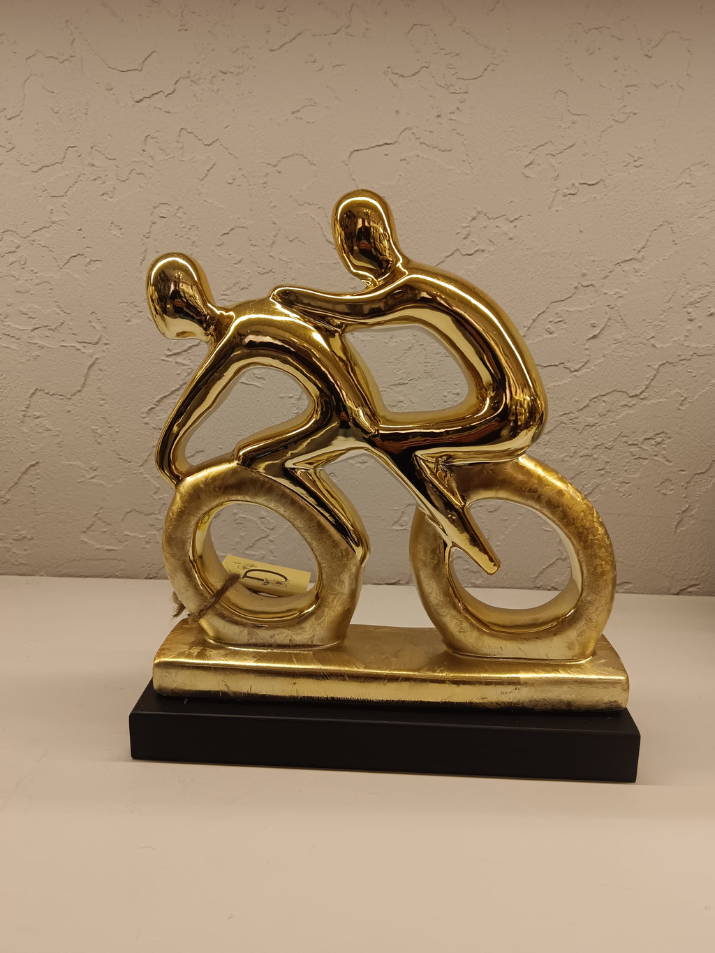 Stylized golden sculpture of two abstract human figures riding bicycles