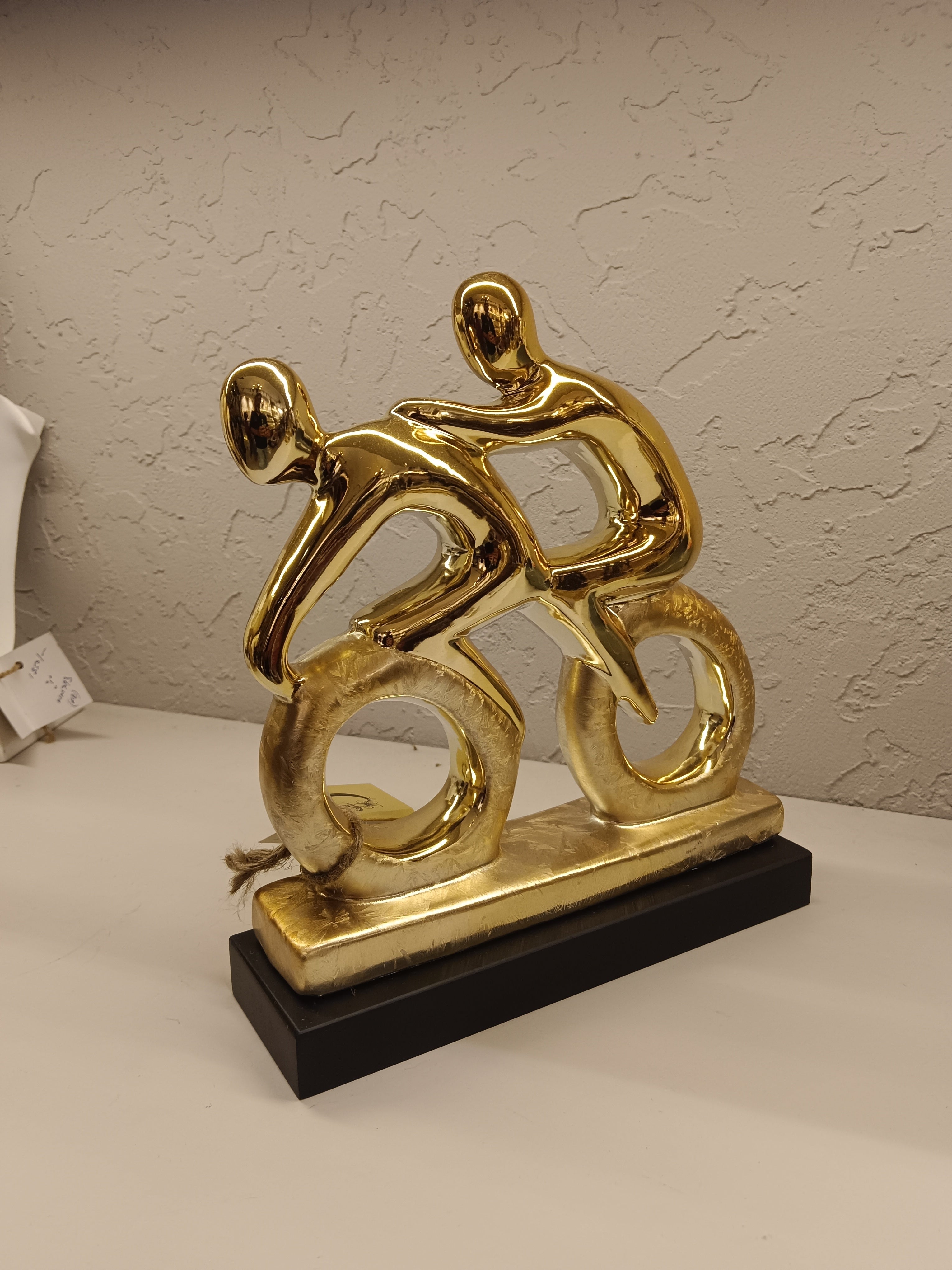 Stylized golden sculpture of two abstract human figures riding bicycles