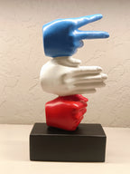 The sculpture features three stylized hands stacked vertically, with each hand