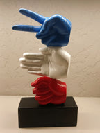 The sculpture features three stylized hands stacked vertically, with each hand