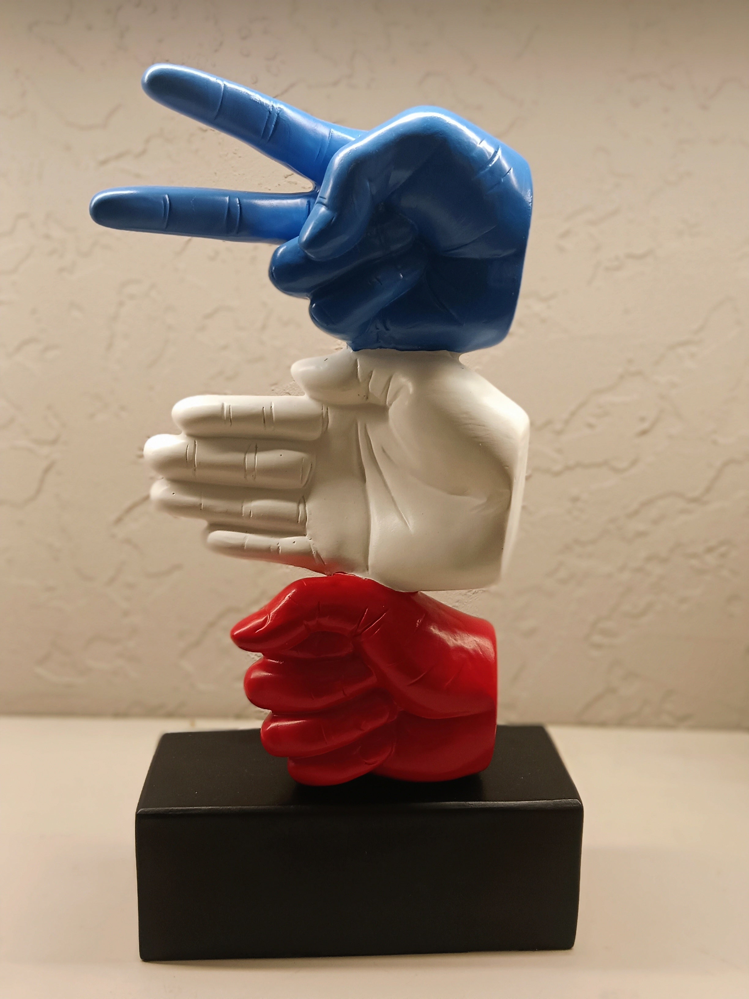 The sculpture features three stylized hands stacked vertically, with each hand