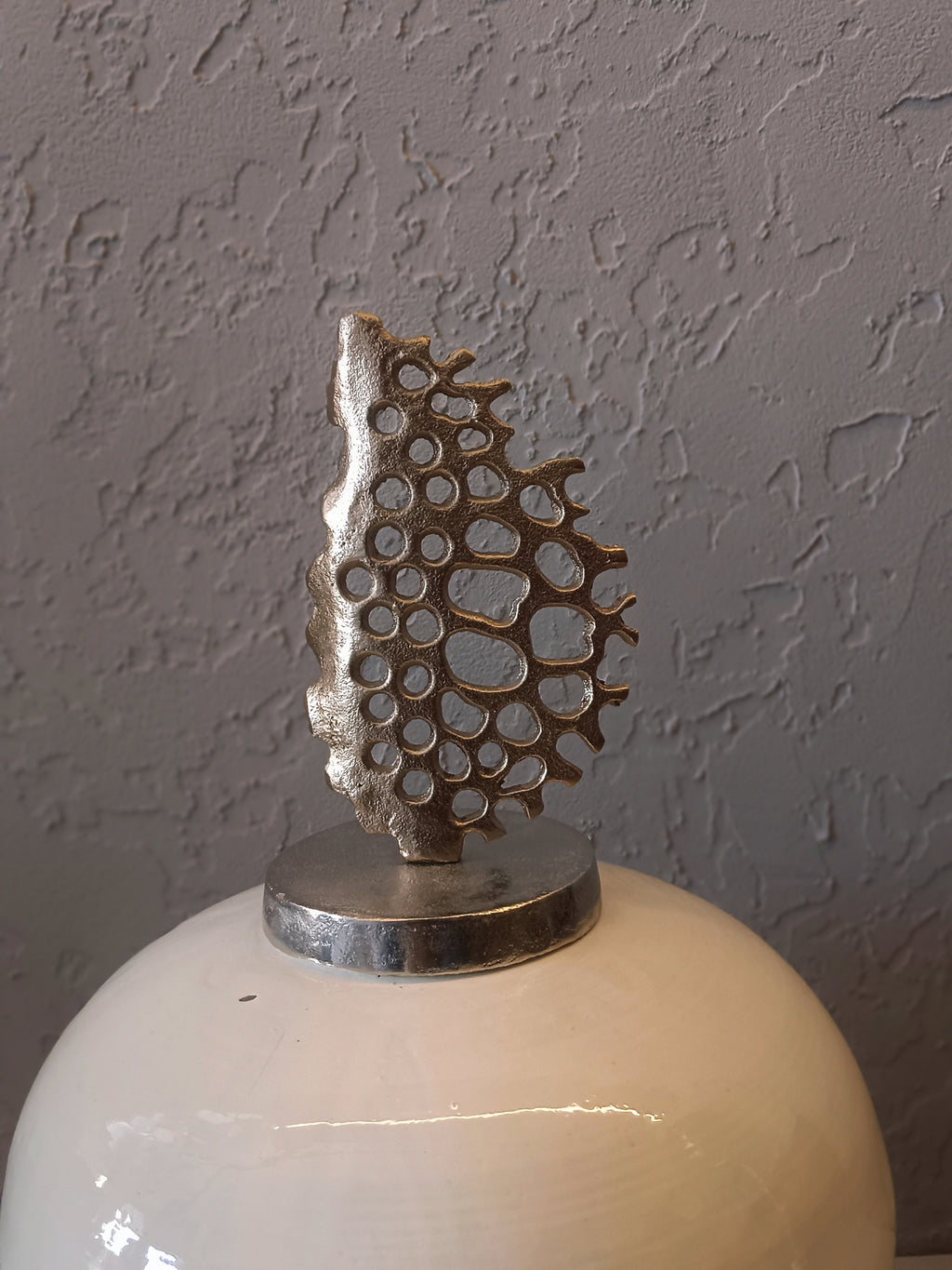 A refined decorative metal vase with a glossy white finish, accented by soft navy brush patterns and crowned with an artistic metallic coral-inspired top