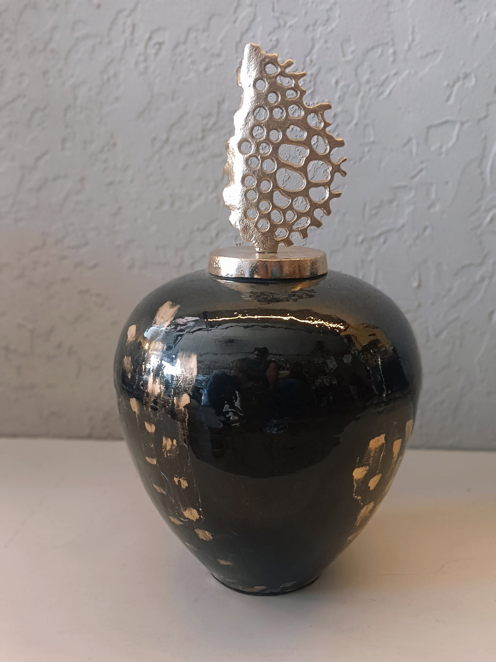 A striking decorative metal vase featuring a glossy black finish with gold accents, topped with an artistic metallic coral-inspired sculpture
