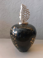 A striking decorative metal vase featuring a glossy black finish with gold accents, topped with an artistic metallic coral-inspired sculpture