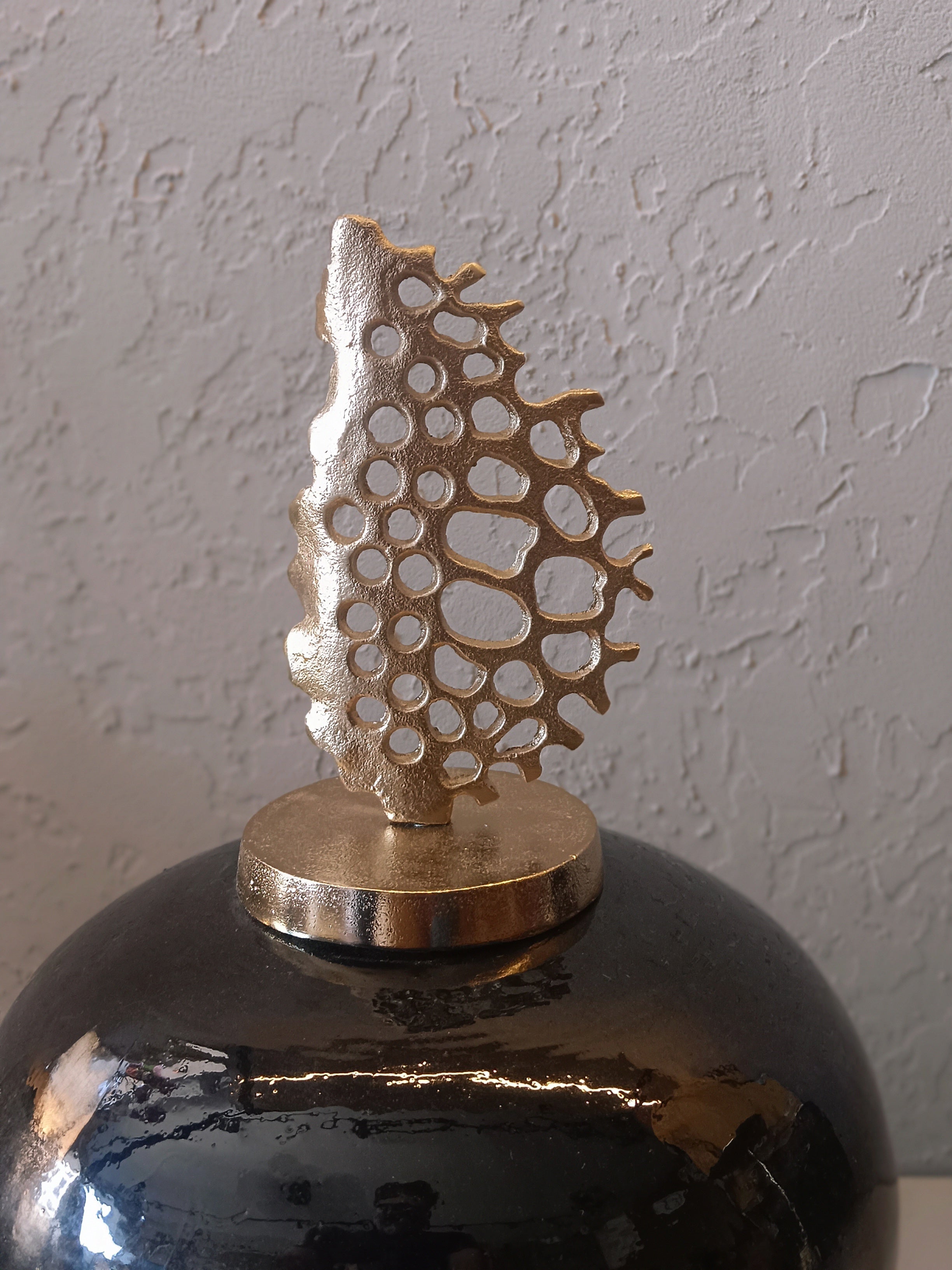 A striking decorative metal vase featuring a glossy black finish with gold accents, topped with an artistic metallic coral-inspired sculpture